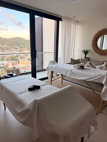 Two massage tables with white linens in a bright suite with floor-to-ceiling windows and an island view in St. Maarten