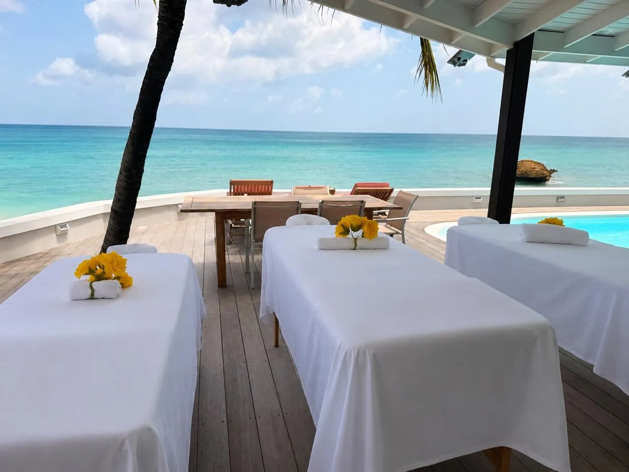 Three oceanfront massage tables dressed in white linens with yellow roses, overlooking the turquoise Caribbean Sea in St. Maarten