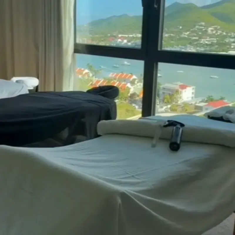 Professional spa setting at luxury vacation rentals in The Hills Residence, St. Maarten Three massage tables set up in a serene spa room at The Hills Residence in St. Maarten, with large windows overlooking Simpson Bay and surrounding hills.