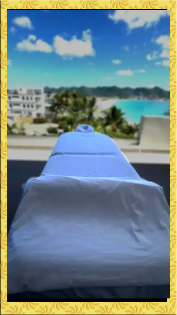 sxm massage table in beacon-hill with white sheets is set on a balcony overlooking a scenic beach view.